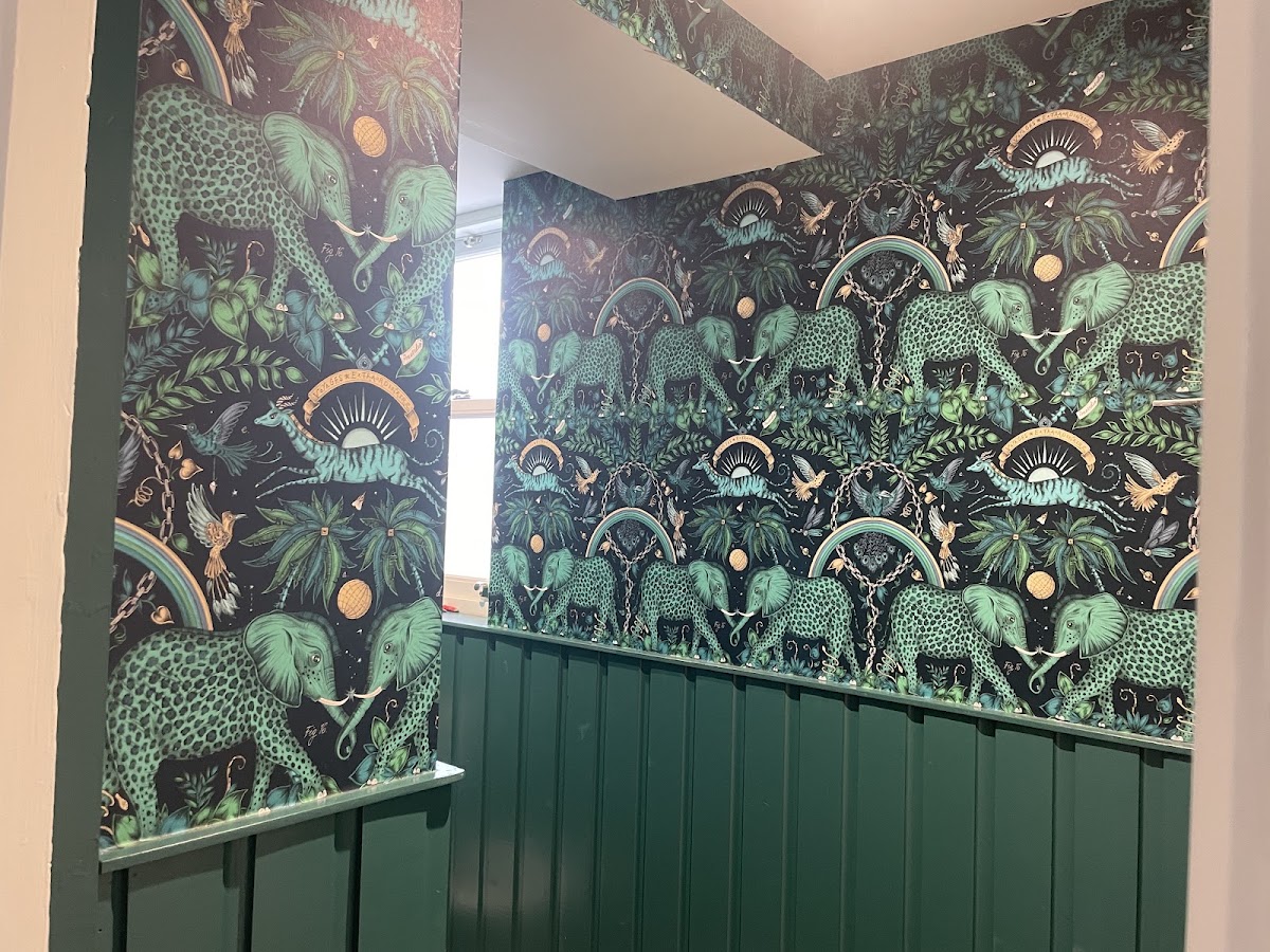 Emerald botanical wallpaper hung above dark green panelling