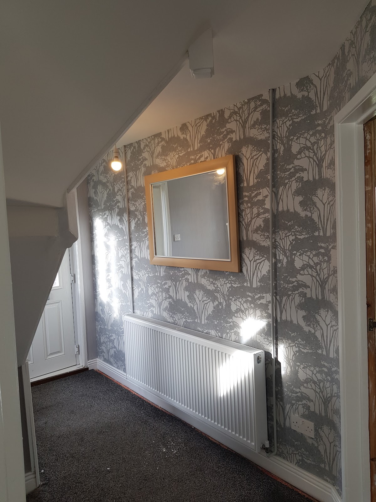 Hallway papered in a grey forest print, hung around a door and eaves